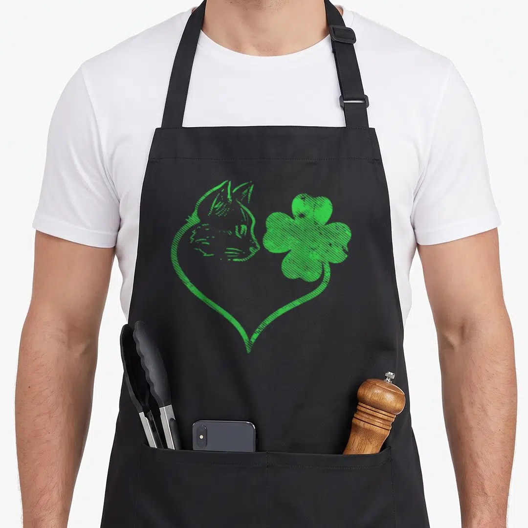 Silhouette pet apron - Green line art of cat head and four-leaf clover merging into a heart shape — shown on a black cotton canvas apron against a white background