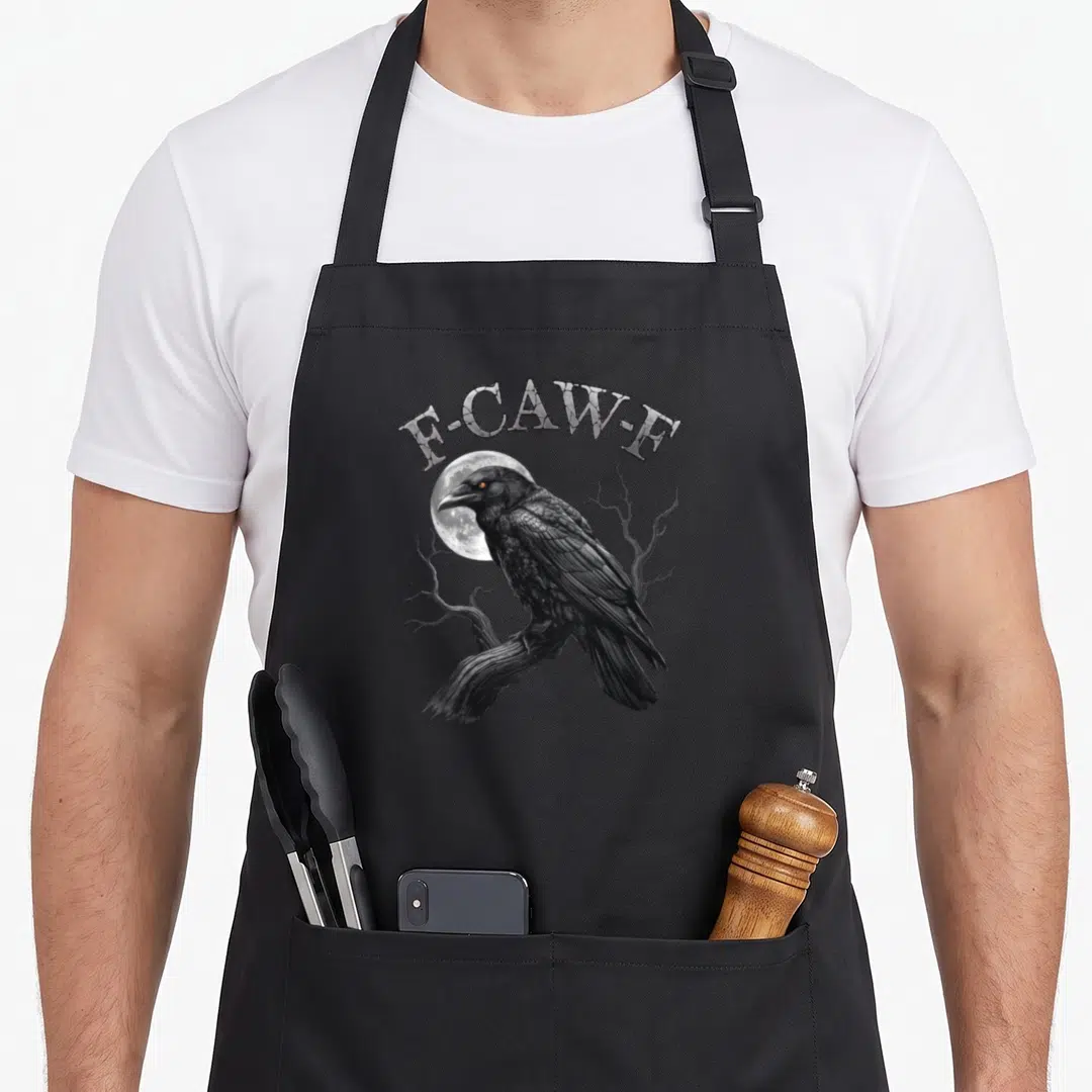 Caw crow halloween apron - F-CAW-F text arched over a realistic black crow perched on a branch in front of a white full — shown on a black cotton canvas apron against a white background