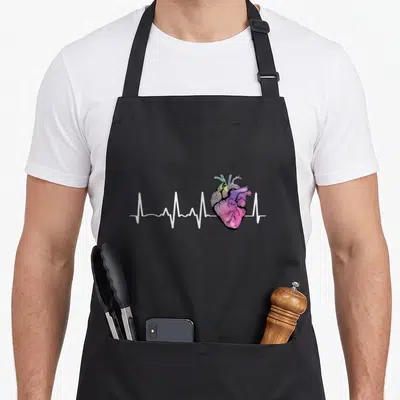 Heartbeat anatomical apron - Watercolor anatomical heart in purple pink green and yellow with white EKG line — shown on a black cotton canvas apron against a white background