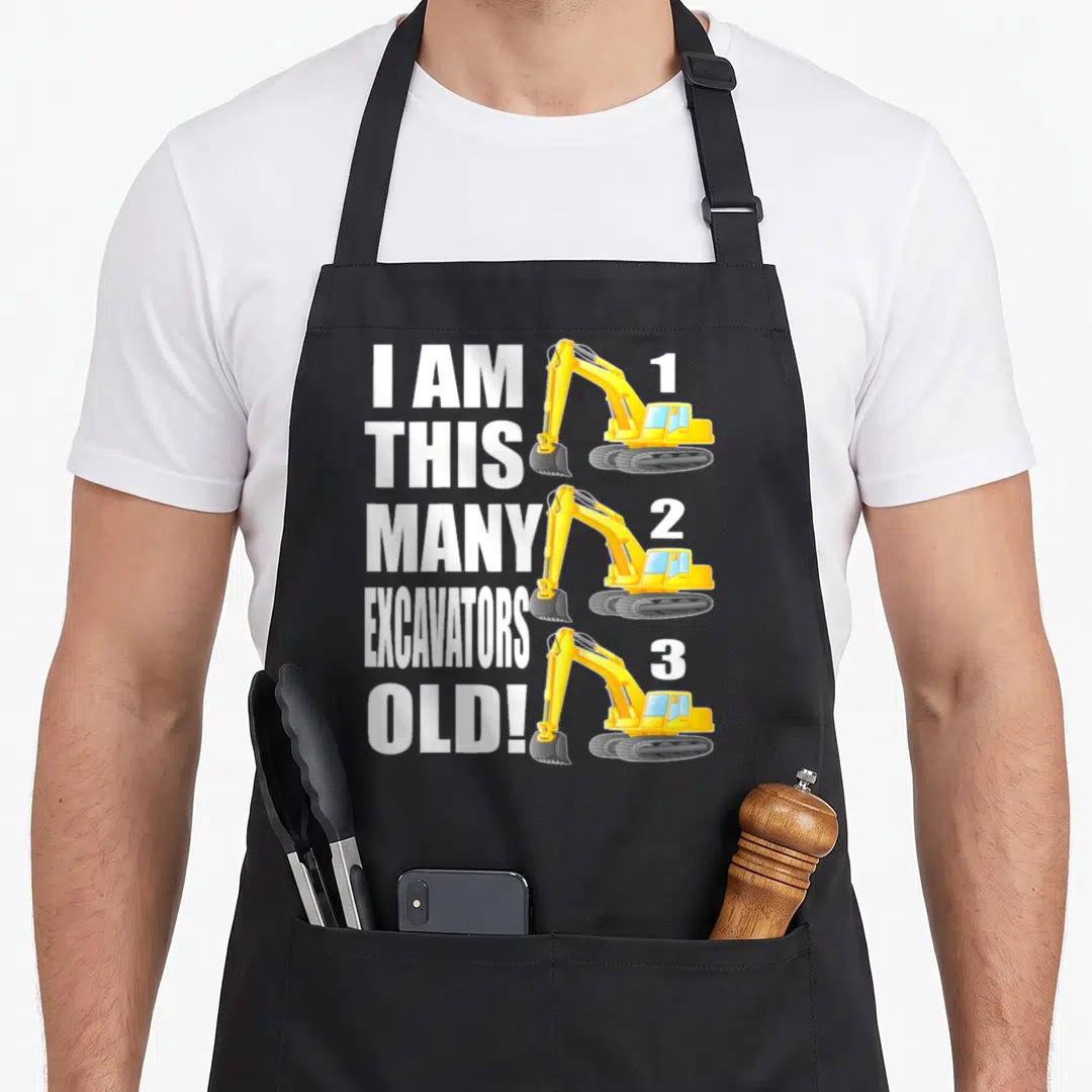 3rd many birthday apron - Three yellow excavators stacked vertically beside white text reading I AM THIS MANY — shown on a black cotton canvas apron against a white background