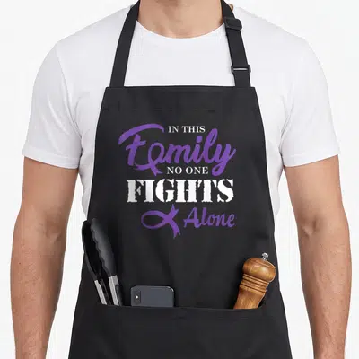 Pancreas cancer girl apron - Purple and white stacked text reading IN THIS Family NO ONE FIGHTS Alone with awareness — shown on a black cotton canvas apron against a white background