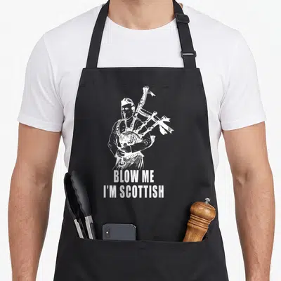 Scottish humorous aprons - White line art bagpiper above blow me i'm scottish text — shown on a black cotton canvas apron against a white background