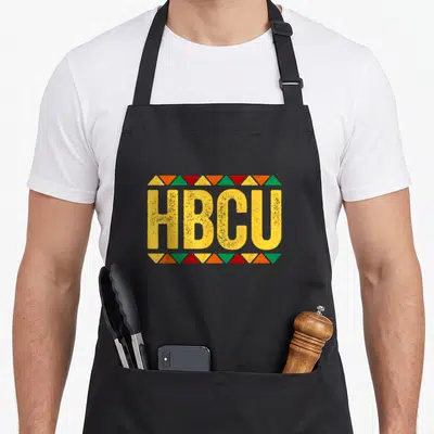 Month historical aprons - HBCU in yellow letters bordered by red green orange and yellow triangles — shown on a black cotton canvas apron against a white background