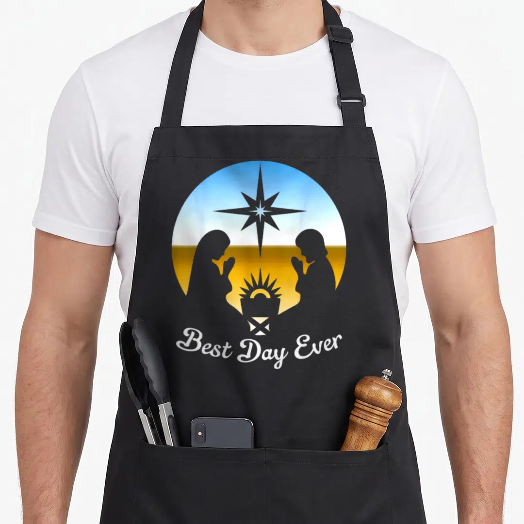 Jesus nativity christmas apron - Grey silhouettes of Mary and Joseph at a manger under a star with Best Day Ever text — shown on a black cotton canvas apron against a white background