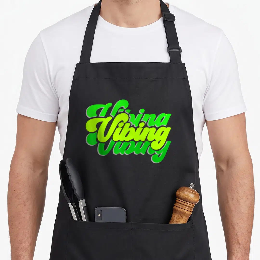 Vibing novelty apron - Stacked green and lime green Vibing typography design on apron front — shown on a black cotton canvas apron against a white background