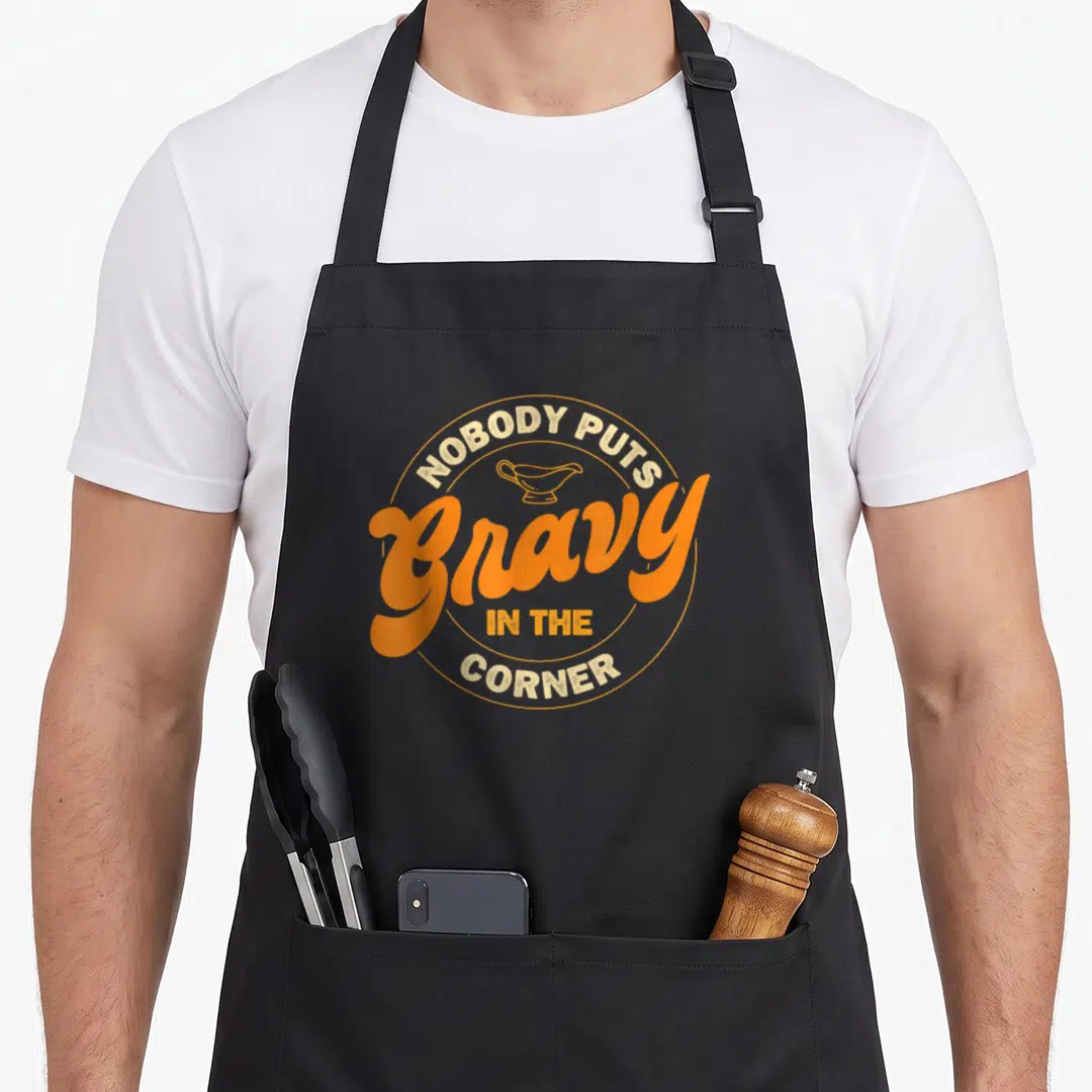 Nobody thanksgiving apron - Retro orange and tan graphic of a gravy boat with arched text reading Nobody Puts Gravy — shown on a black cotton canvas apron against a white background