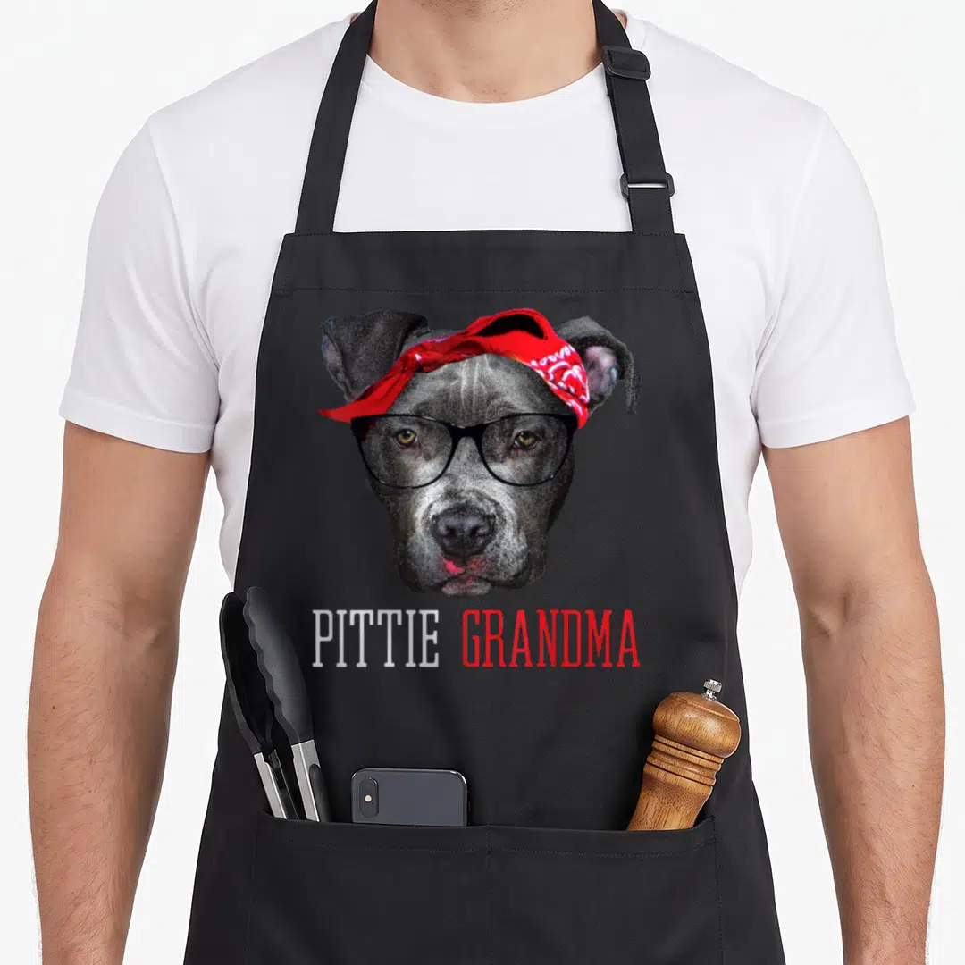 Pittie granny apron - Grey dog head wearing black glasses and red bandana with PITTIE GRANDMA text — shown on a black cotton canvas apron against a white background