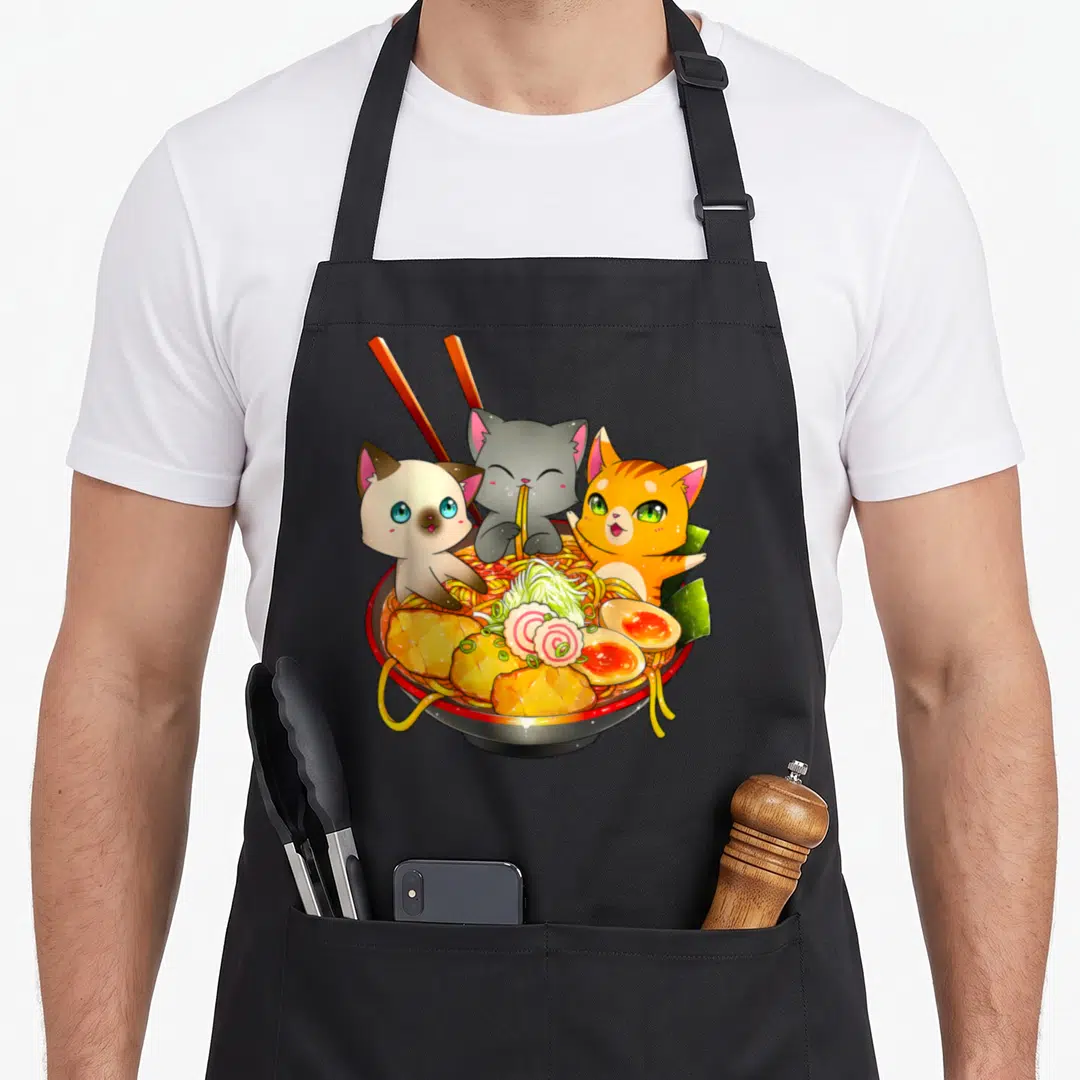 Ramen kawaii cat apron - Three cartoon cats inside a ramen bowl with chopsticks and toppings — shown on a black cotton canvas apron against a white background
