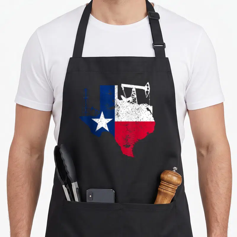 Oilfield patriotic apron - Distressed Texas state flag map with blue oil derrick and white pumpjack silhouettes — shown on a black cotton canvas apron against a white background
