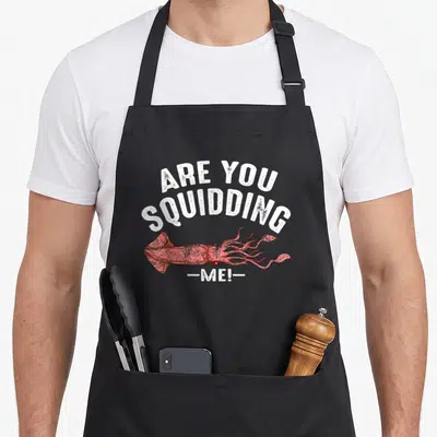 Squidding fish apron - Red squid illustration with arched white text reading are you squidding me in distressed font — shown on a black cotton canvas apron against a white background
