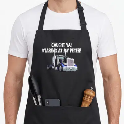Caught semi truck apron - Distressed white text CAUGHT YA STARING AT MY PETER above a blue silver semi-truck — shown on a black cotton canvas apron against a white background