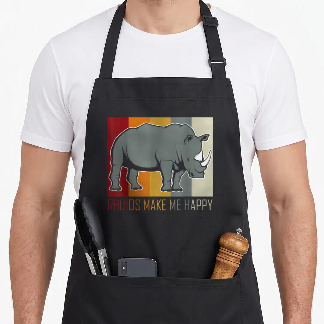 Cute rhino apron - Grey rhino over five vertical stripes with matching colored text reading rhinos make me happy — shown on a black cotton canvas apron against a white background