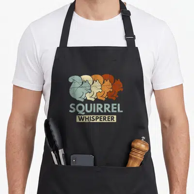 Whisperer forest animal apron - Four overlapping squirrels in blue-grey, beige, orange, and reddish-brown with stacked — shown on a black cotton canvas apron against a white background
