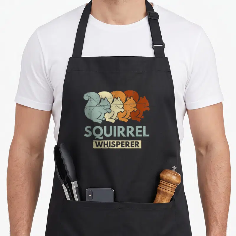 Whisperer forest animal apron - Four overlapping squirrels in blue-grey, beige, orange, and reddish-brown with stacked — shown on a black cotton canvas apron against a white background