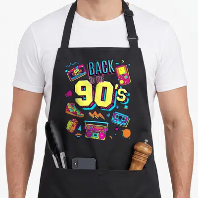 Cute 90s apron - Retro graphic with BACK TO THE 90's text, boombox, cassettes, and game console in yellow pink blue cyan — shown on a black cotton canvas apron against a white background