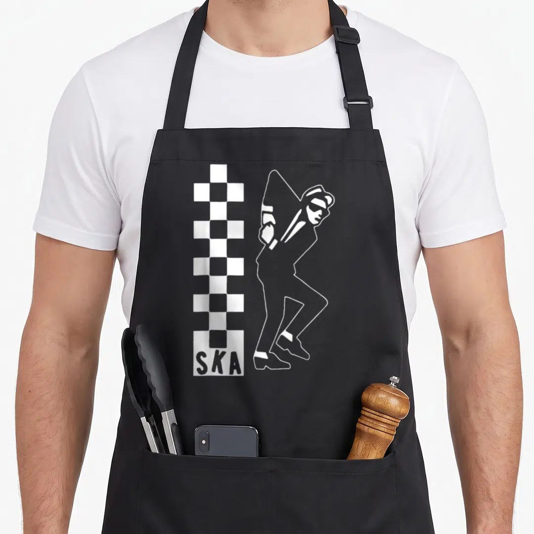 Reggae ska quotes apron - White outline of a musician beside a checkerboard column with SKA text at the base — shown on a black cotton canvas apron against a white background