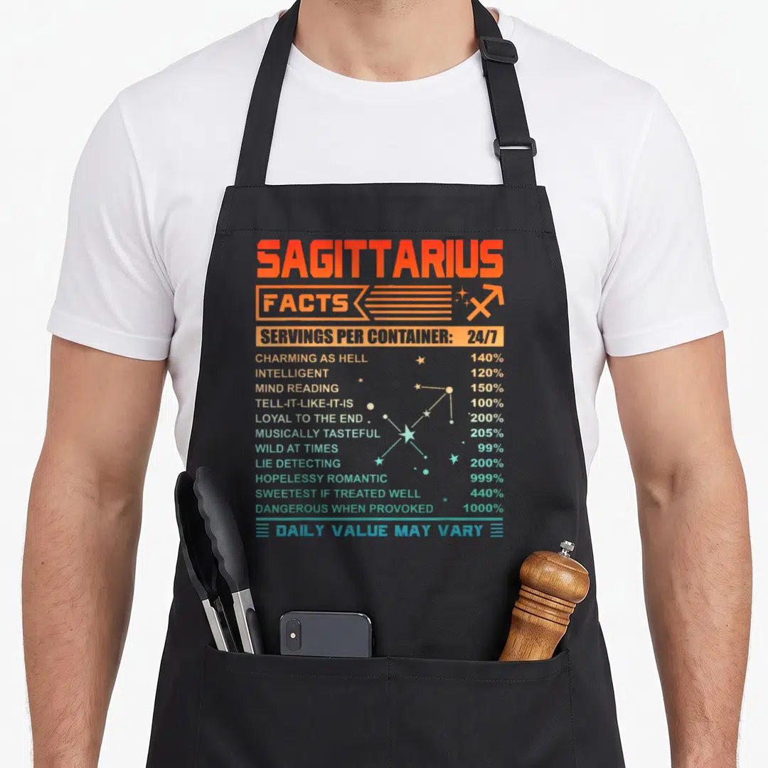 Sagittarius fact birthday apron - Orange and blue nutrition facts label style print listing Sagittarius traits — shown on a black cotton canvas apron against a white background
