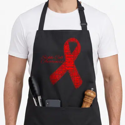 Sickle ribbon apron - Red awareness ribbon formed by hope fight cure word cloud with Sickle Cell Awareness text — shown on a black cotton canvas apron against a white background