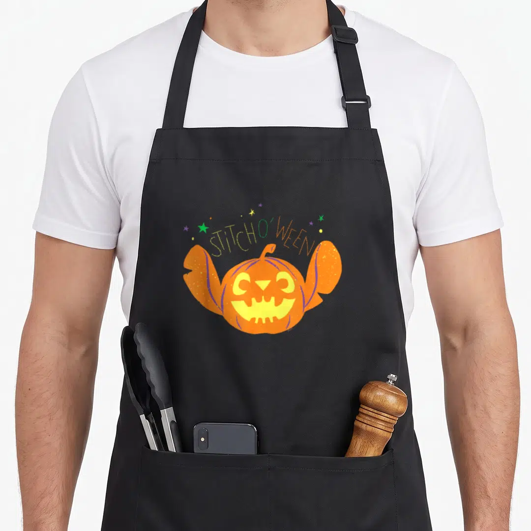 Ween halloween apron - STITCH O WEEN text over orange alien pumpkin with stars — shown on a black cotton canvas apron against a white background