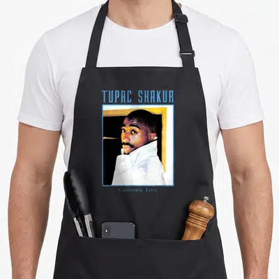 Eye tupac apron - Tupac Shakur framed portrait with California Love text in blue and yellow — shown on a black cotton canvas apron against a white background