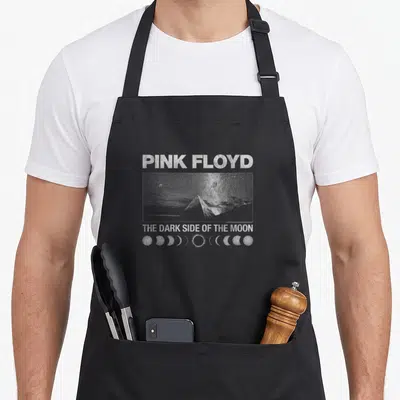 Floyd moon vintage apron - White pyramid, moon phases, and Pink Floyd text on black fabric — shown on a black cotton canvas apron against a white background
