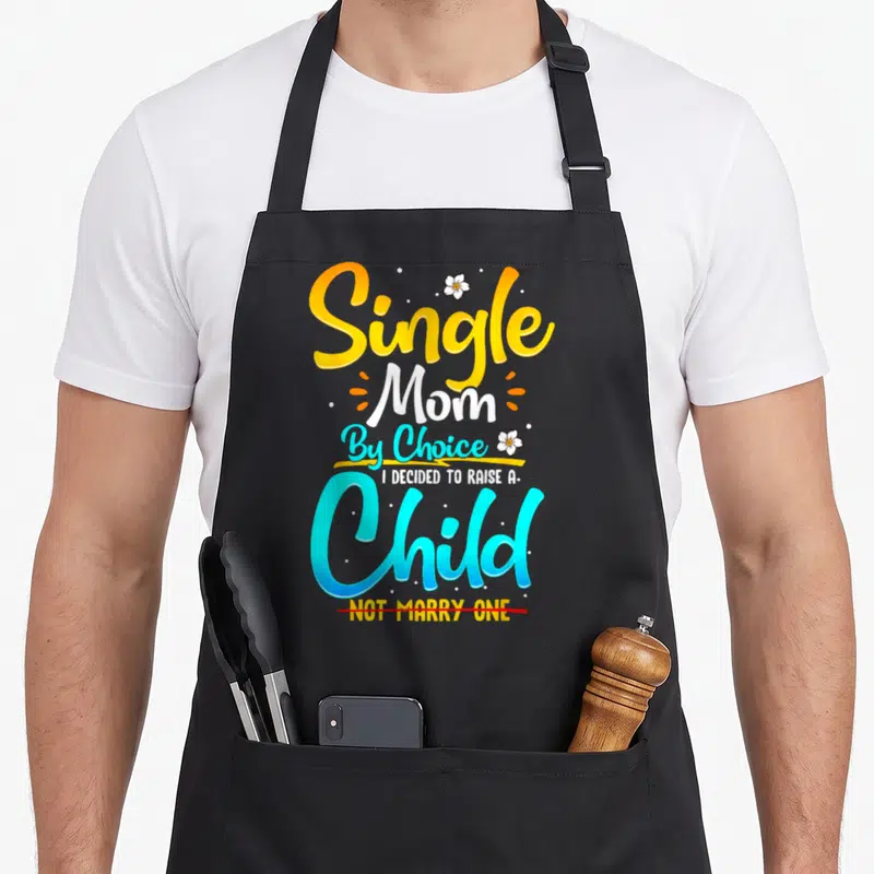 Single choice aprons - Stacked Single Mom By Choice text in yellow cyan white with red strikethrough and flowers — shown on a black cotton canvas apron against a white background