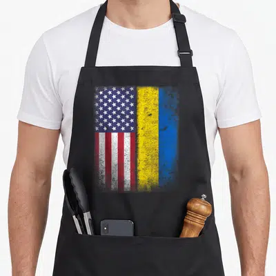 Cute ukrainian american flag apron - Distressed USA and Ukraine flags side by side in blue white red and yellow — shown on a black cotton canvas apron against a white background