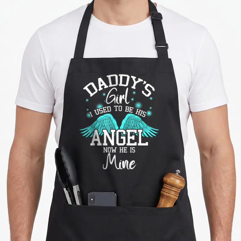 Daddy angels in aprons - White stacked text DADDY'S Girl I USED TO BE HIS ANGEL NOW HE IS Mine with cyan wings — shown on a black cotton canvas apron against a white background