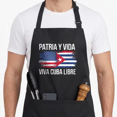 Country cuba american flag apron - Split US and Cuban flag with distressed paint and white text PATRIA Y VIDA VIVA CUBA — shown on a black cotton canvas apron against a white background