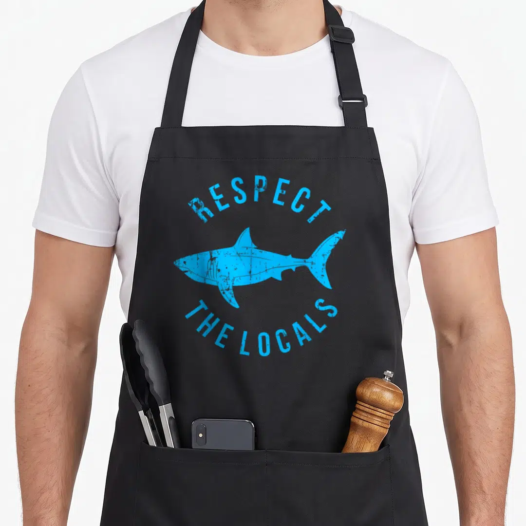 Respect animal apron - Blue retro shark silhouette with arched text RESPECT THE LOCALS — shown on a black cotton canvas apron against a white background