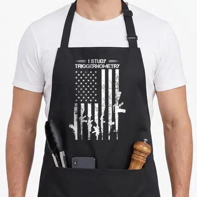 Study american flag apron - I Study Triggernometry text with rifles replacing flag stripes in distressed white — shown on a black cotton canvas apron against a white background