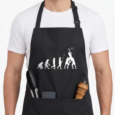 Evolution rugby apron - White silhouettes showing evolution of man ending with two rugby players jumping for an oval — shown on a black cotton canvas apron against a white background