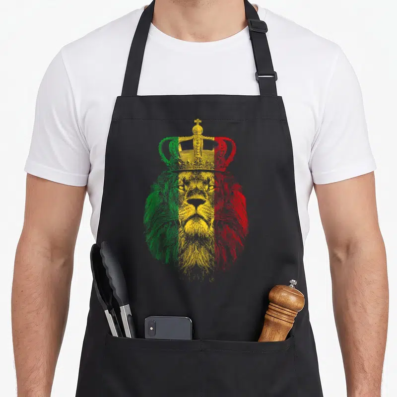 Rasta lion apron - Line-art lion head with crown filled with vertical green, yellow, and red bands — shown on a black cotton canvas apron against a white background