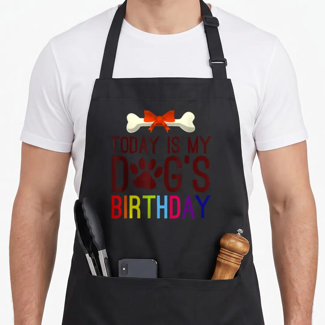 Today custom pet apron - Bone with red bow above stacked text TODAY IS MY DOG'S BIRTHDAY with rainbow letters and paw — shown on a black cotton canvas apron against a white background