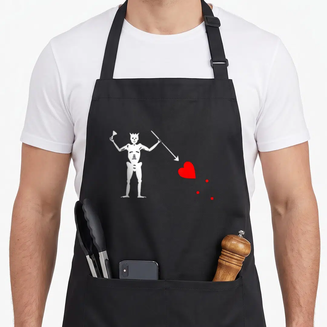 North earl grey apron - White skeleton holding cup and arrow pointing to red heart with three dots — shown on a black cotton canvas apron against a white background