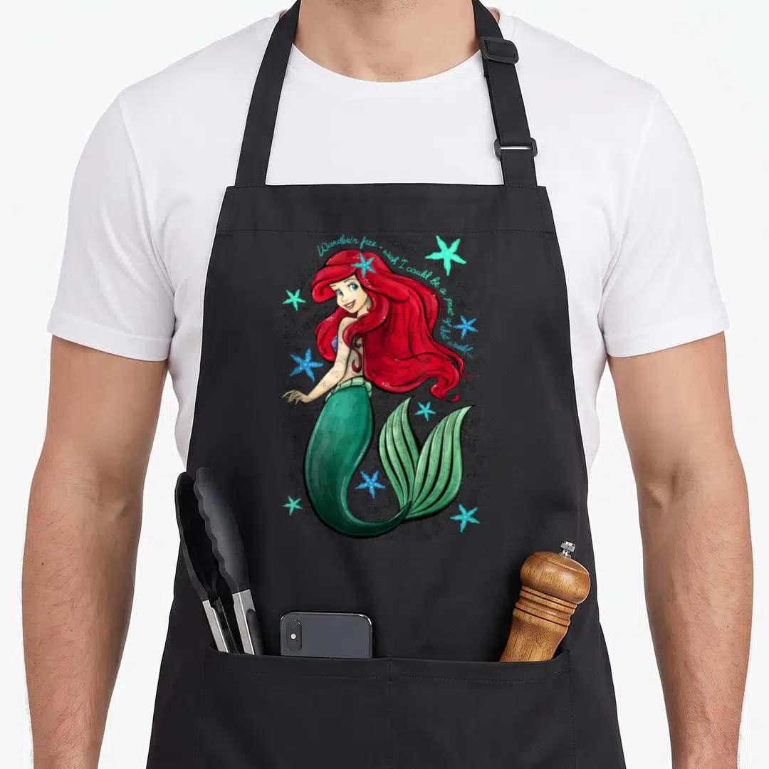 Song mermaid apron - Cartoon mermaid with red hair, teal starfish, and arched script text on grey background — shown on a black cotton canvas apron against a white background