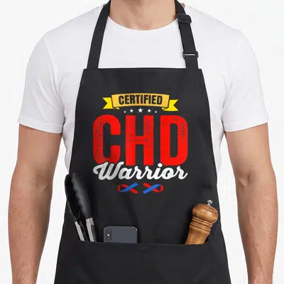 Survivor congenital heart defect apron - Certified CHD Warrior text with yellow banner, five stars, and two red blue — shown on a black cotton canvas apron against a white background