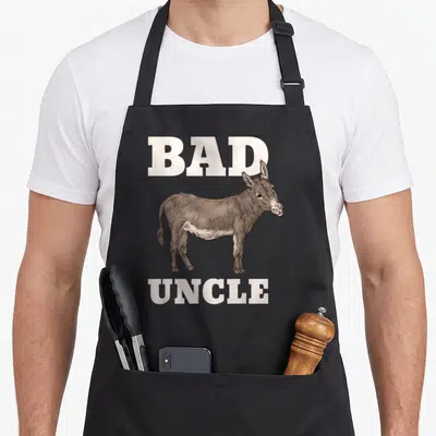 Uncle badass apron - Realistic brown donkey centered between BAD and UNCLE text on grey background — shown on a black cotton canvas apron against a white background