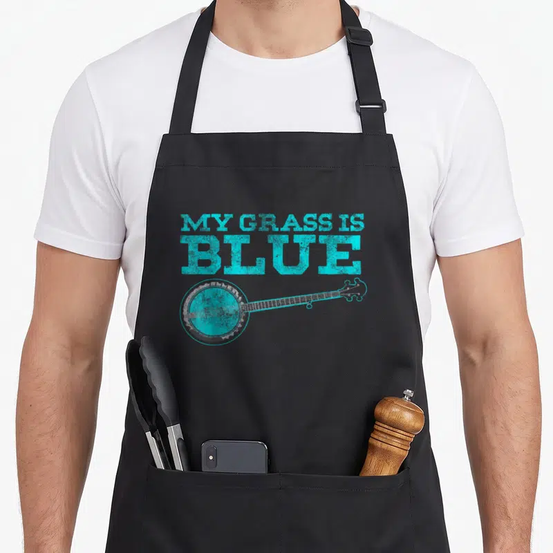 Grass banjo apron - Cyan text MY GRASS IS BLUE above a grey distressed banjo lying horizontally — shown on a black cotton canvas apron against a white background