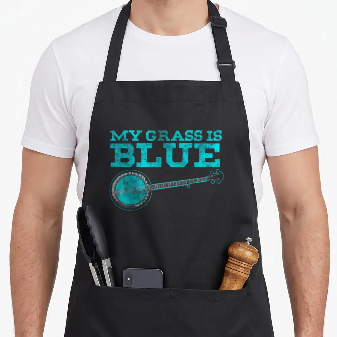 Grass banjo apron - Cyan text MY GRASS IS BLUE above a grey distressed banjo lying horizontally — shown on a black cotton canvas apron against a white background