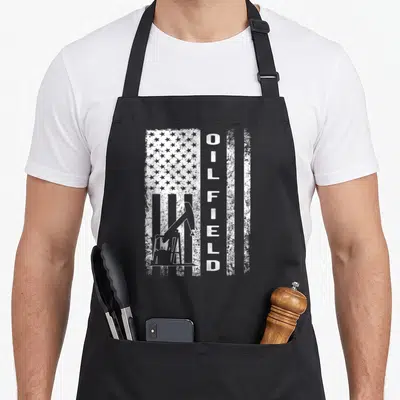 Oil field apron - White distressed vertical flag with pump jack and vertical OILFIELD text — shown on a black cotton canvas apron against a white background