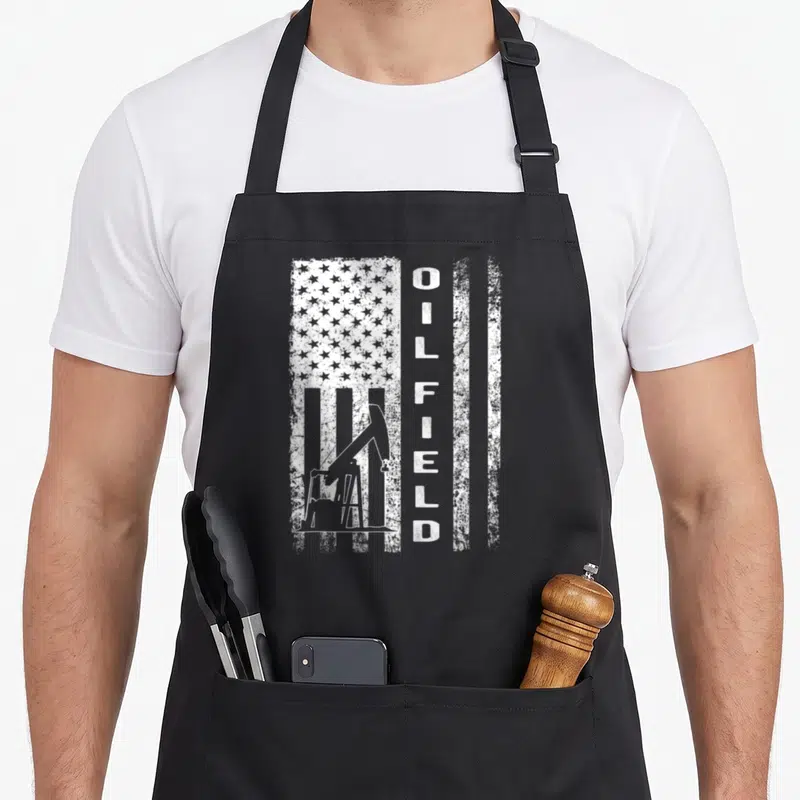 Oil field apron - White distressed vertical flag with pump jack and vertical OILFIELD text — shown on a black cotton canvas apron against a white background