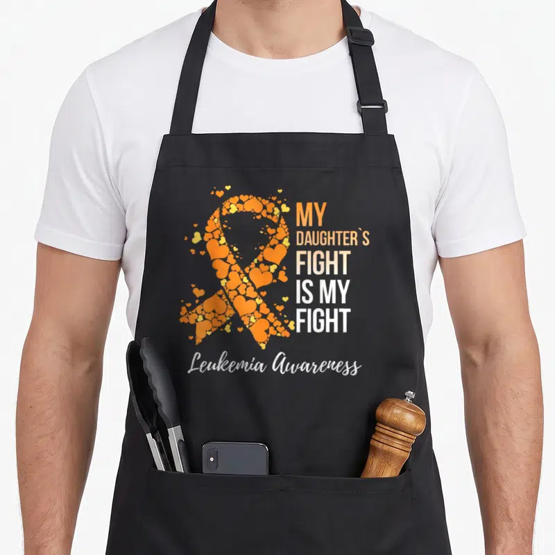 Daughter mothers day apron - Orange ribbon formed by hearts next to My Daughters Fight Is My Fight text and Leukemia — shown on a black cotton canvas apron against a white background