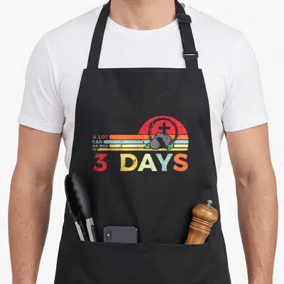 Lot easter apron - Retro sunset with cross, crown of thorns, rock, and text A LOT CAN HAPPEN IN 3 DAYS — shown on a black cotton canvas apron against a white background