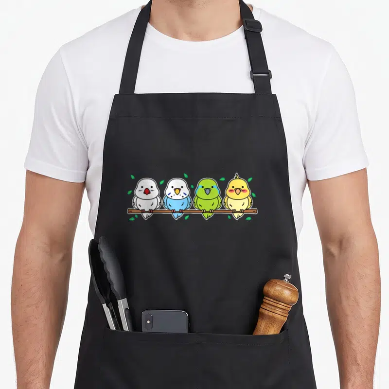 Owner parakeet lover apron - Four cartoon budgies in white blue green yellow brown perched on brown branch with green — shown on a black cotton canvas apron against a white background