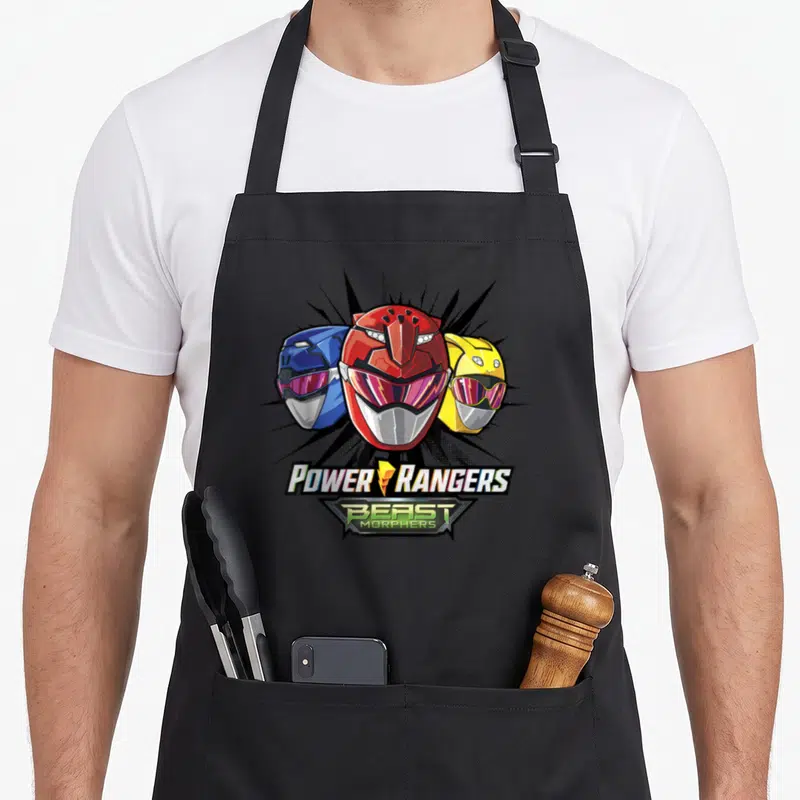 Shot rangers apron - Three red blue and yellow Power Ranger helmets above Beast Morphers logo text — shown on a black cotton canvas apron against a white background