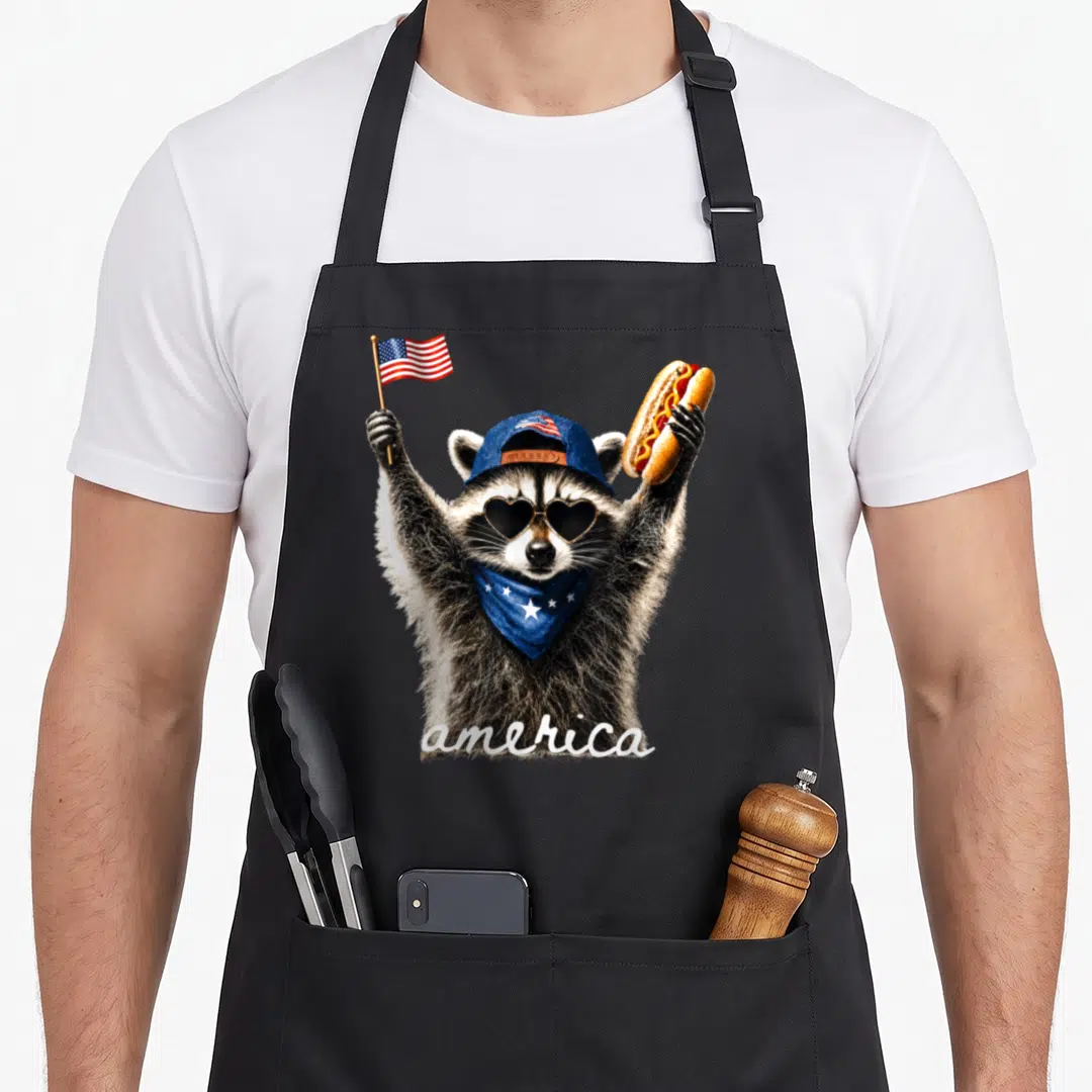 Raccoon hot dog apron - Realistic raccoon holding flag and hot dog with america text and patriotic accessories — shown on a black cotton canvas apron against a white background
