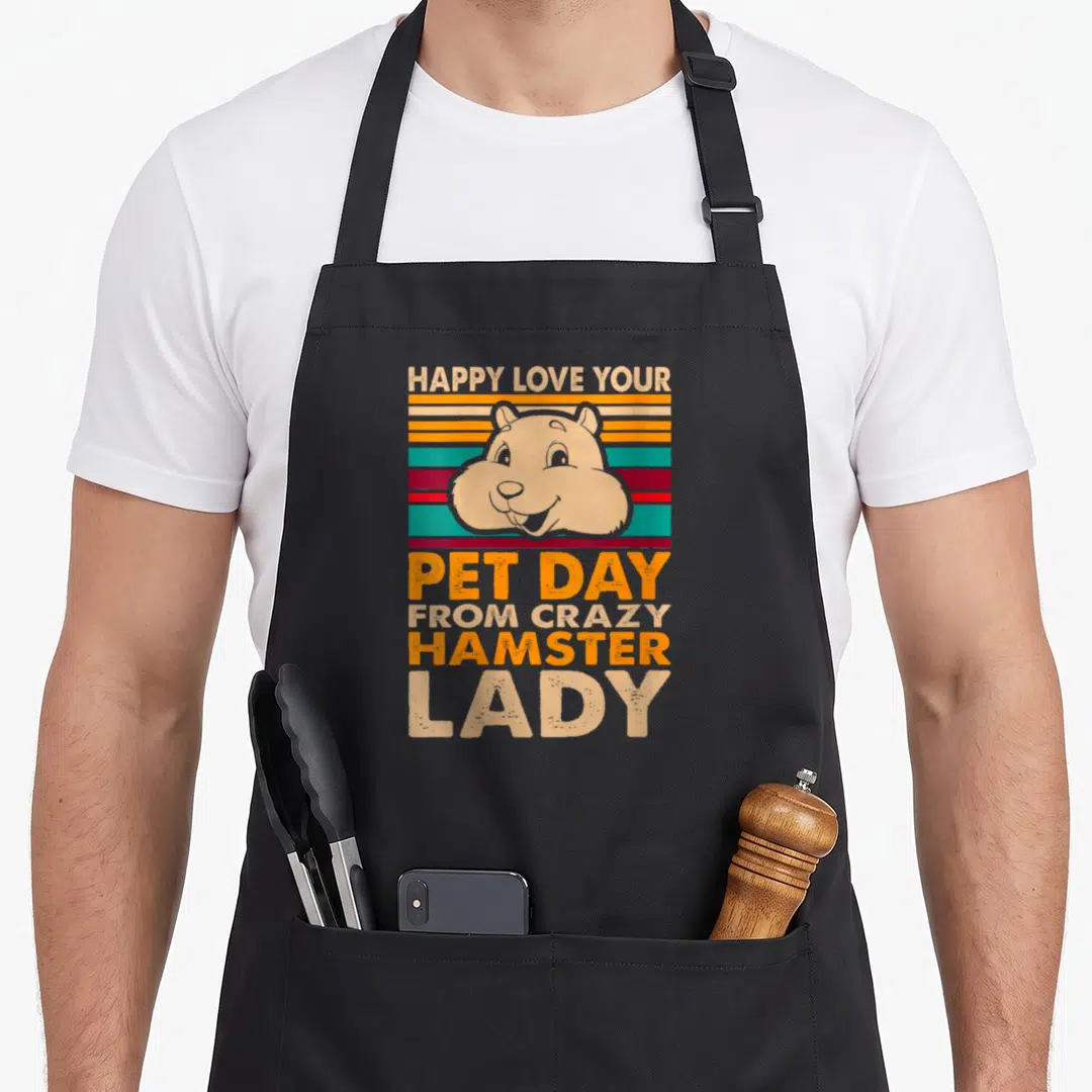 Cute hamster pet apron - Retro tan hamster head over orange teal and red stripes with stacked text reading HAPPY LOVE — shown on a black cotton canvas apron against a white background