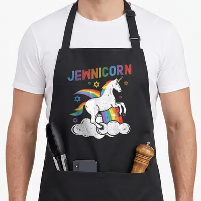 Jewnicorn jewish apron - White unicorn on cloud with rainbow mane and scattered Stars of David under arched — shown on a black cotton canvas apron against a white background