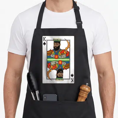 Spade african american aprons - Mirrored King of Spades playing card illustration in red, yellow, green, blue, and gold — shown on a black cotton canvas apron against a white background